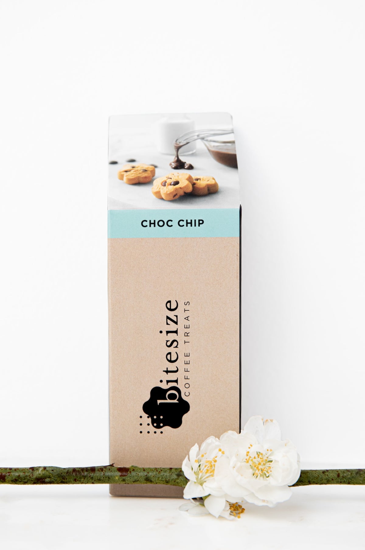 A tall rectangular box of bitesize Coffee Treats Choc Chip coffee chip treats, standing upright on a white surface with a green stem and white flowers in the foreground.