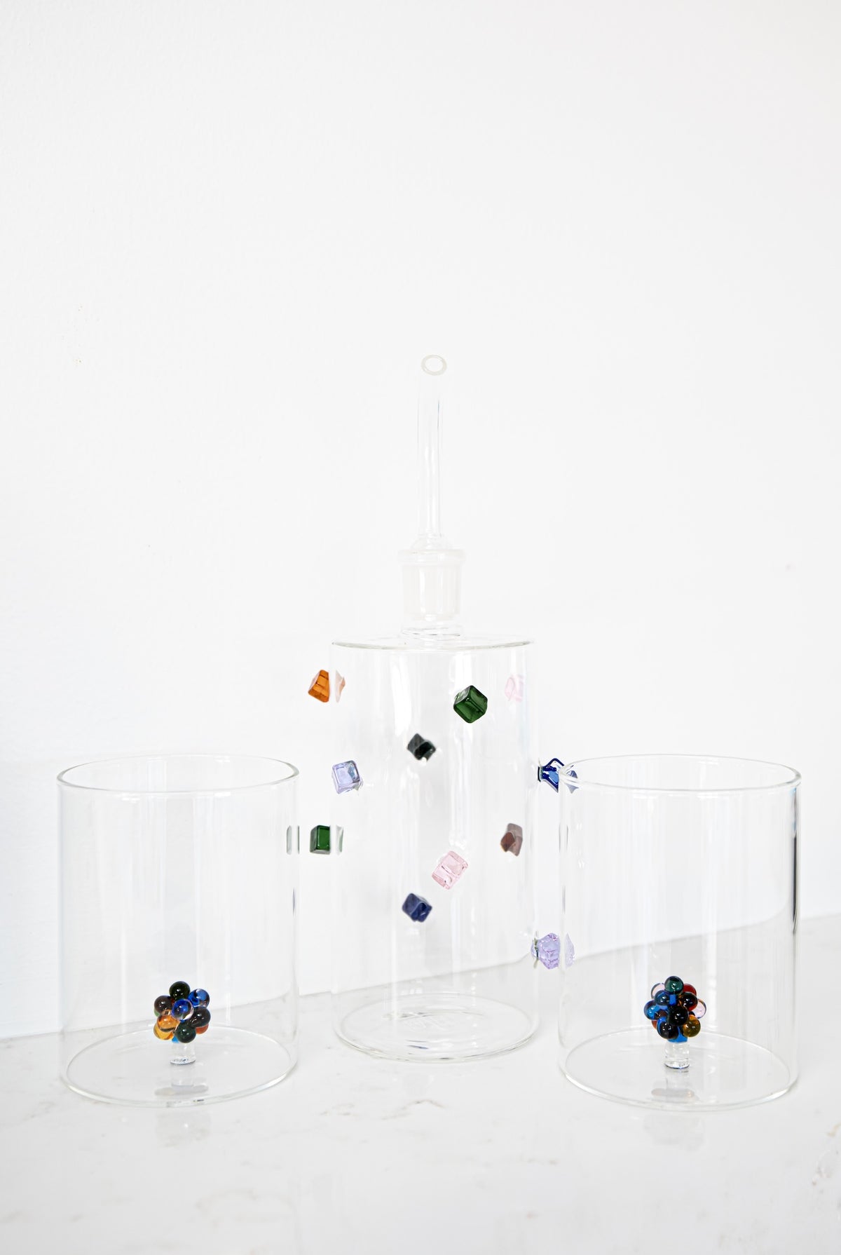 Three clear glass canisters of different sizes on a white marble surface against a white background, decorated with colorful glass beads.