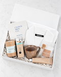 A curated gift box set from Bamboo Handmade and Cloud Skin Co. arranged in a white box with shredded paper filler on a light marble surface.